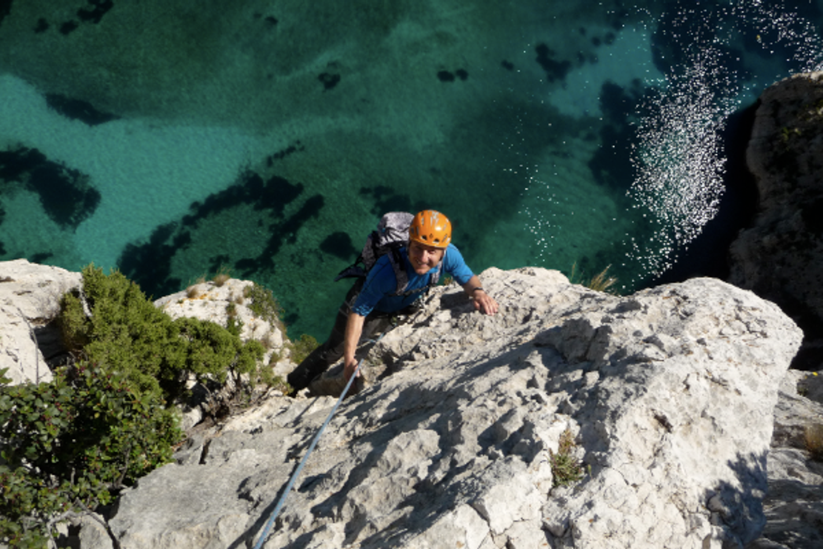 Grimpeur au casque orange sur une paroi blanche dominant les eaux turquoise d’En-Vau