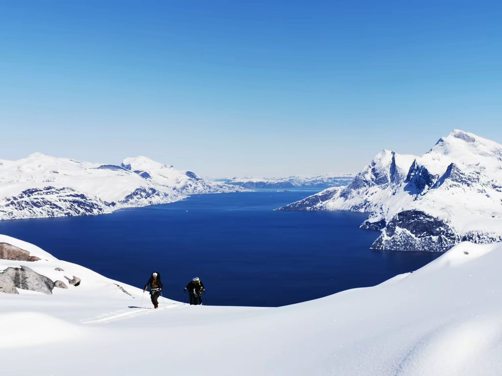 Deux skieurs contemplant un vaste fjord entouré de sommets enneigés au Groenland