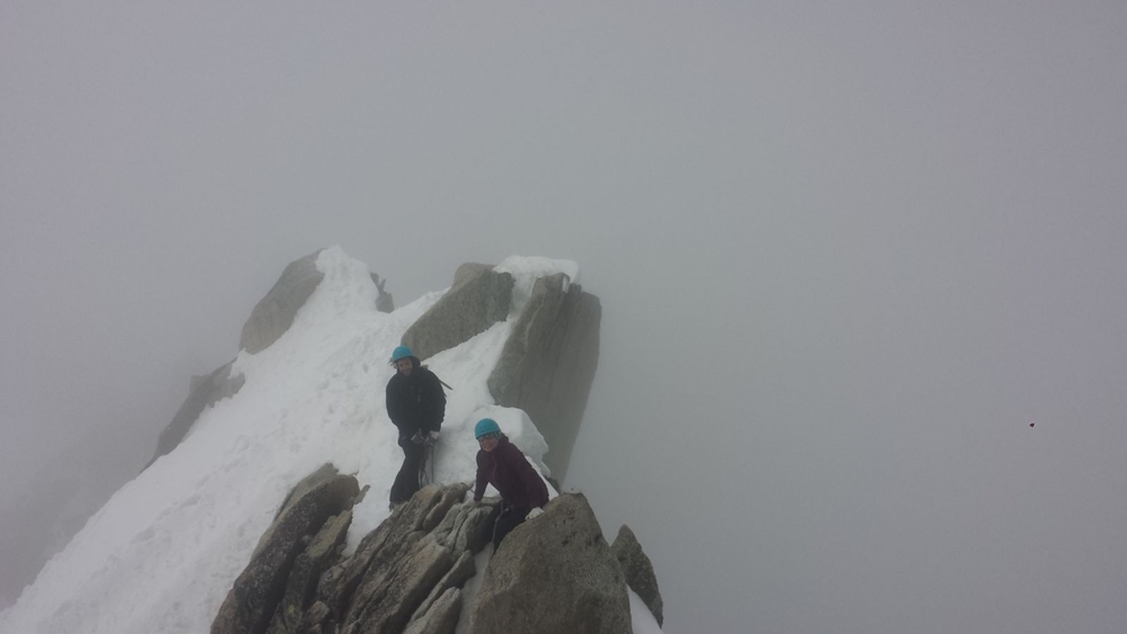 Deux alpinistes progressent entre rochers et neige dans la brume, vers la fin de l’arête des Cosmiques.