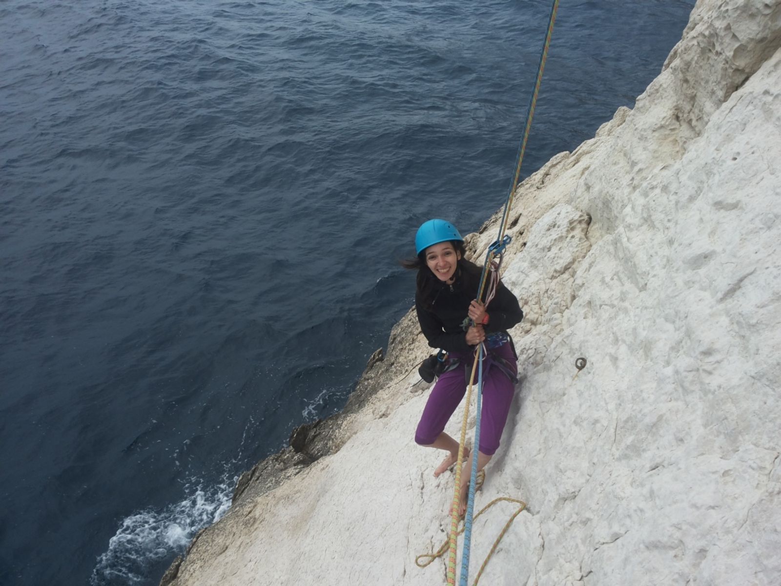 Grimpeuse en pantalon violet sur le calcaire blanc, avec la mer juste en dessous