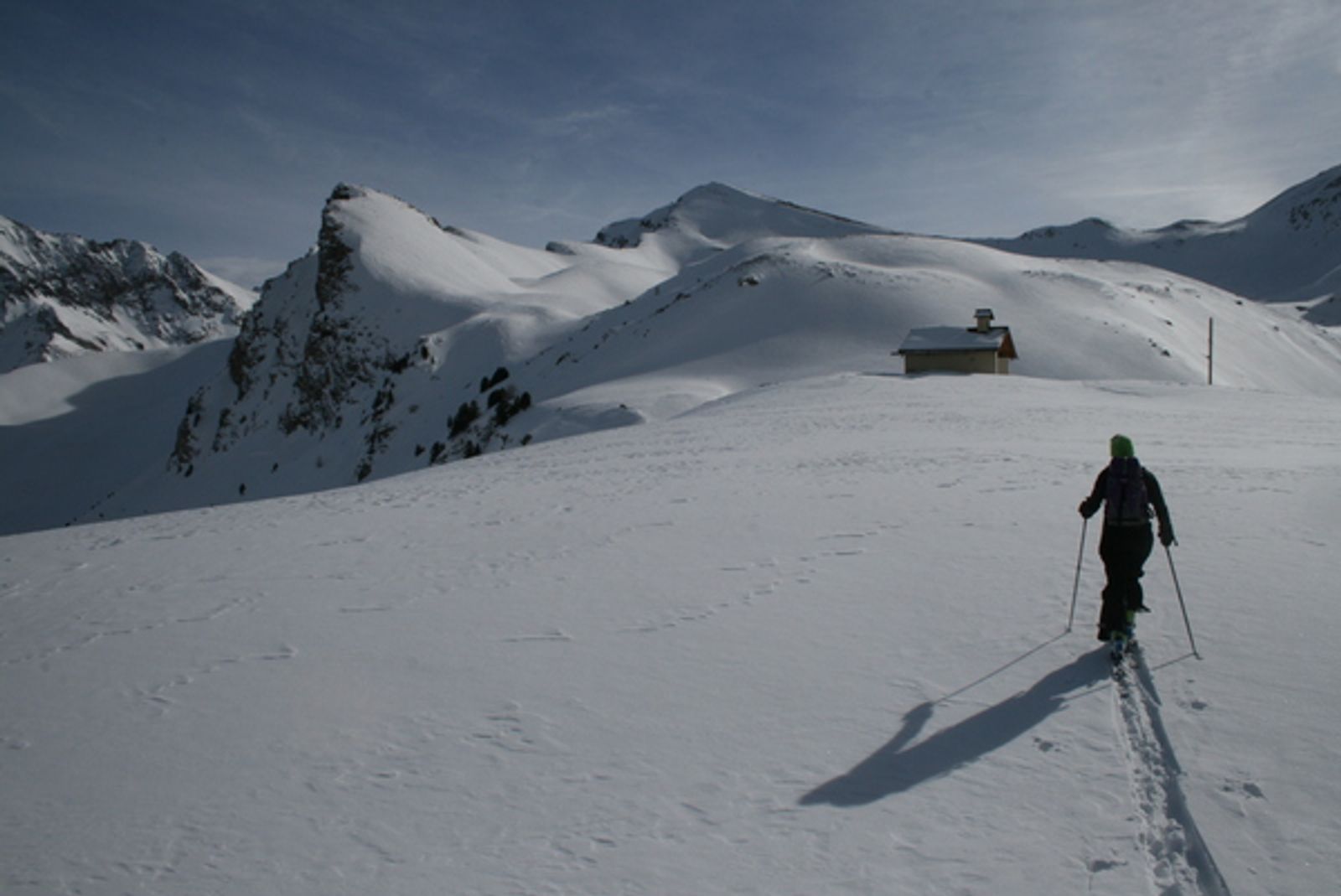 Skieur de randonnée montant vers une cabane sur les pentes enneigées du Girardin.