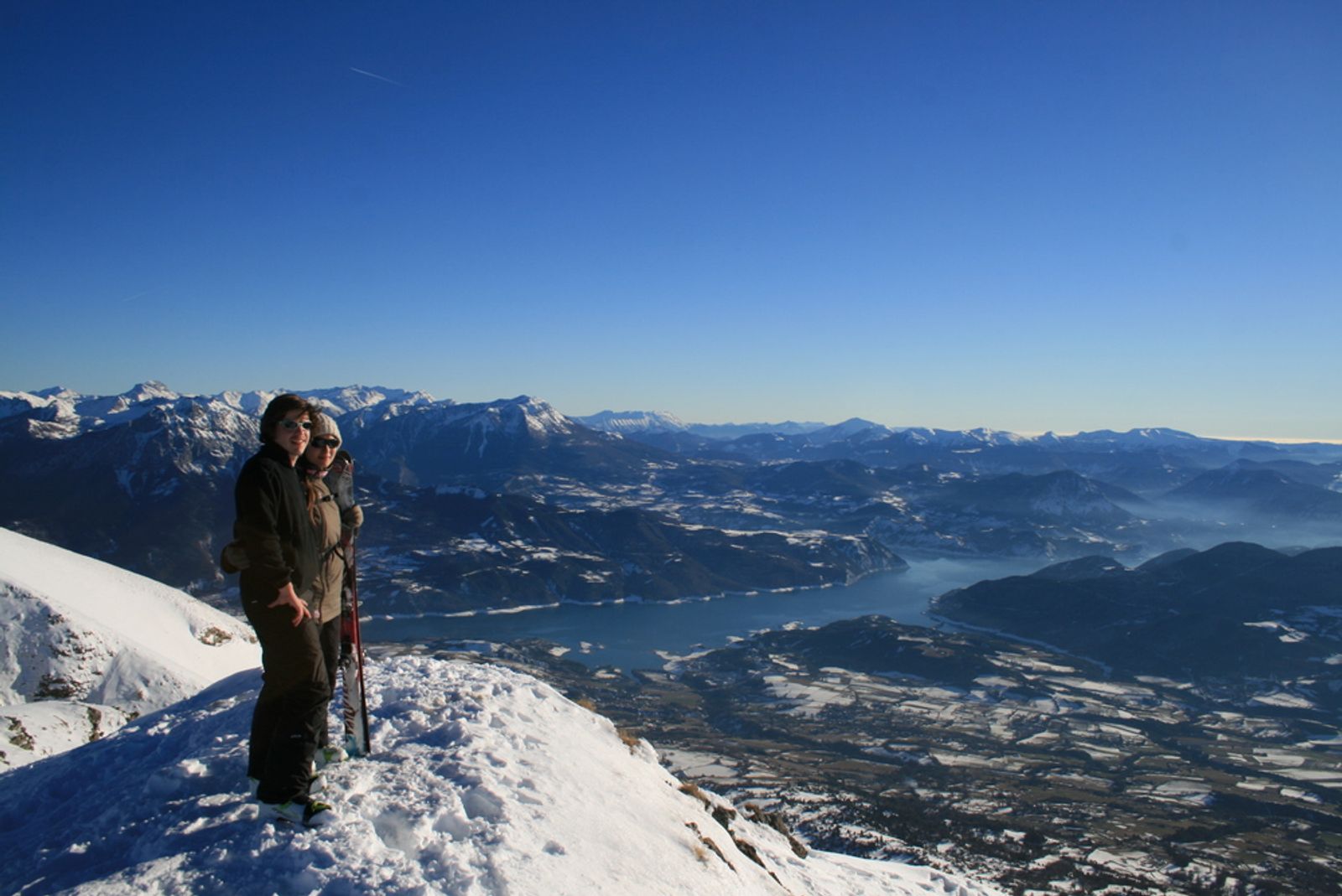 Couple de skieurs sur un sommet devant le lac de Serre ponçon, skis à la main