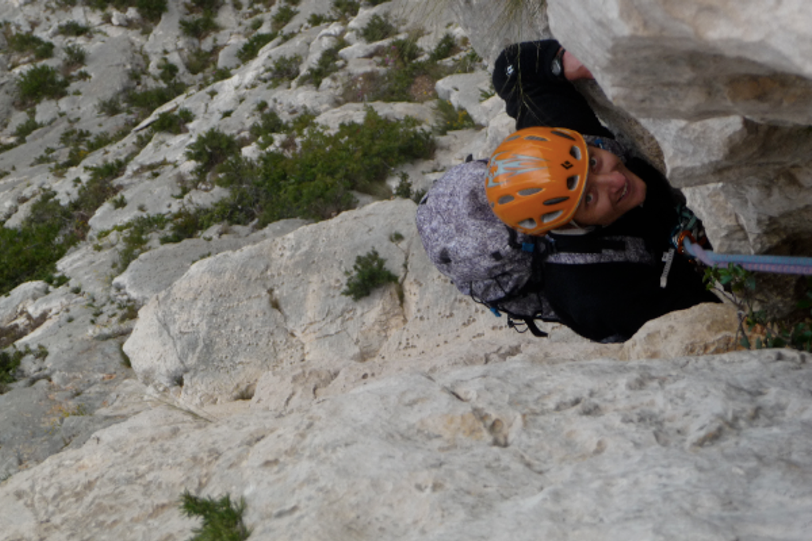 Grimpeur au casque orange engagé dans un passage étroit entre deux parois calcaires