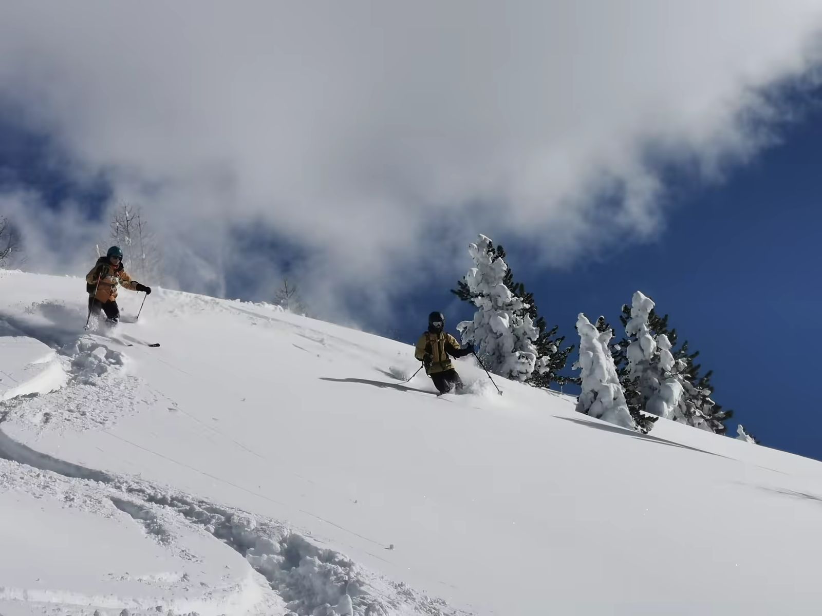 Deux skieurs basculant dans une pente de poudreuse depuis une crête enneigée