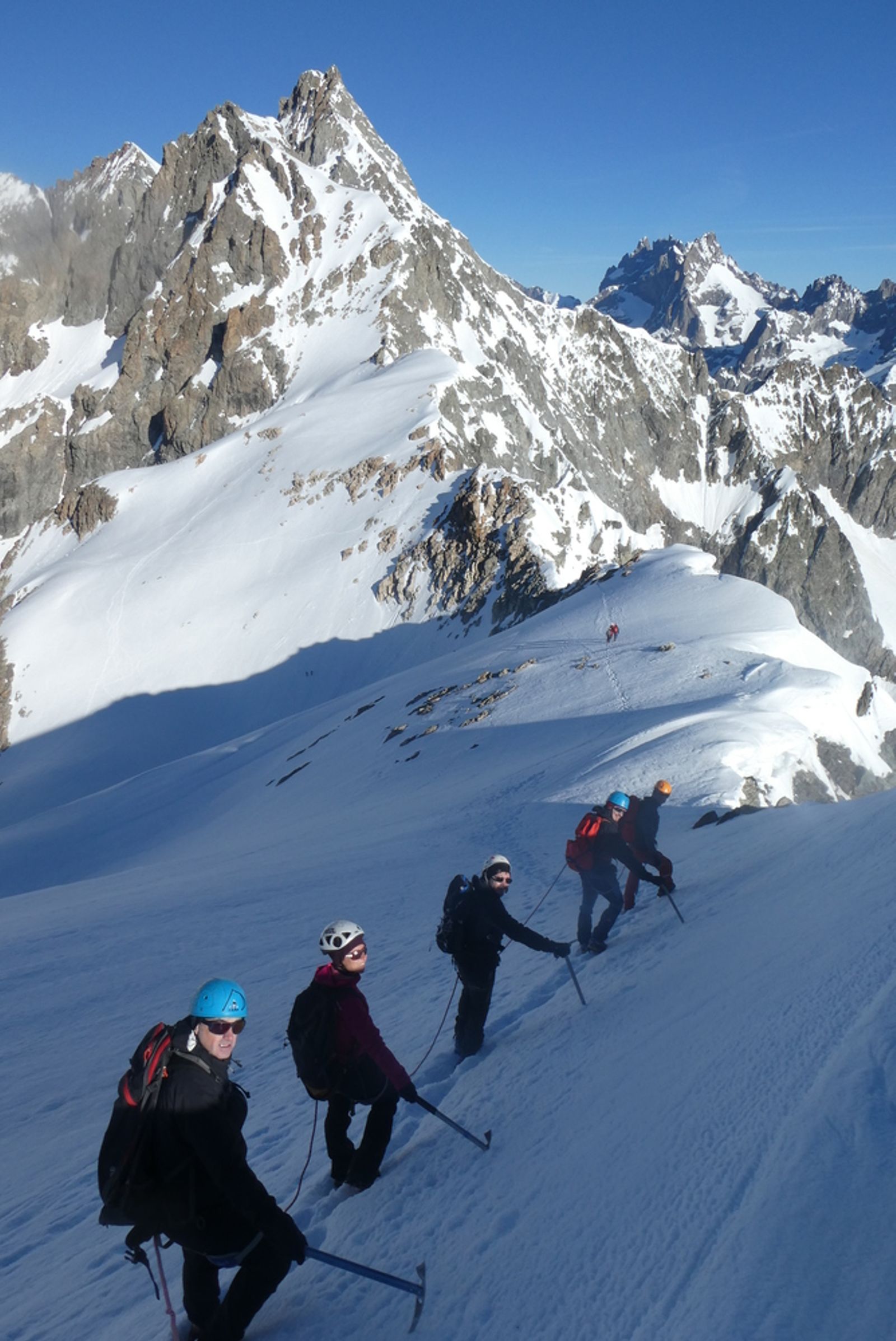 Cordée descendant une pente de neige sous les rochers du Pic d’Arsine.