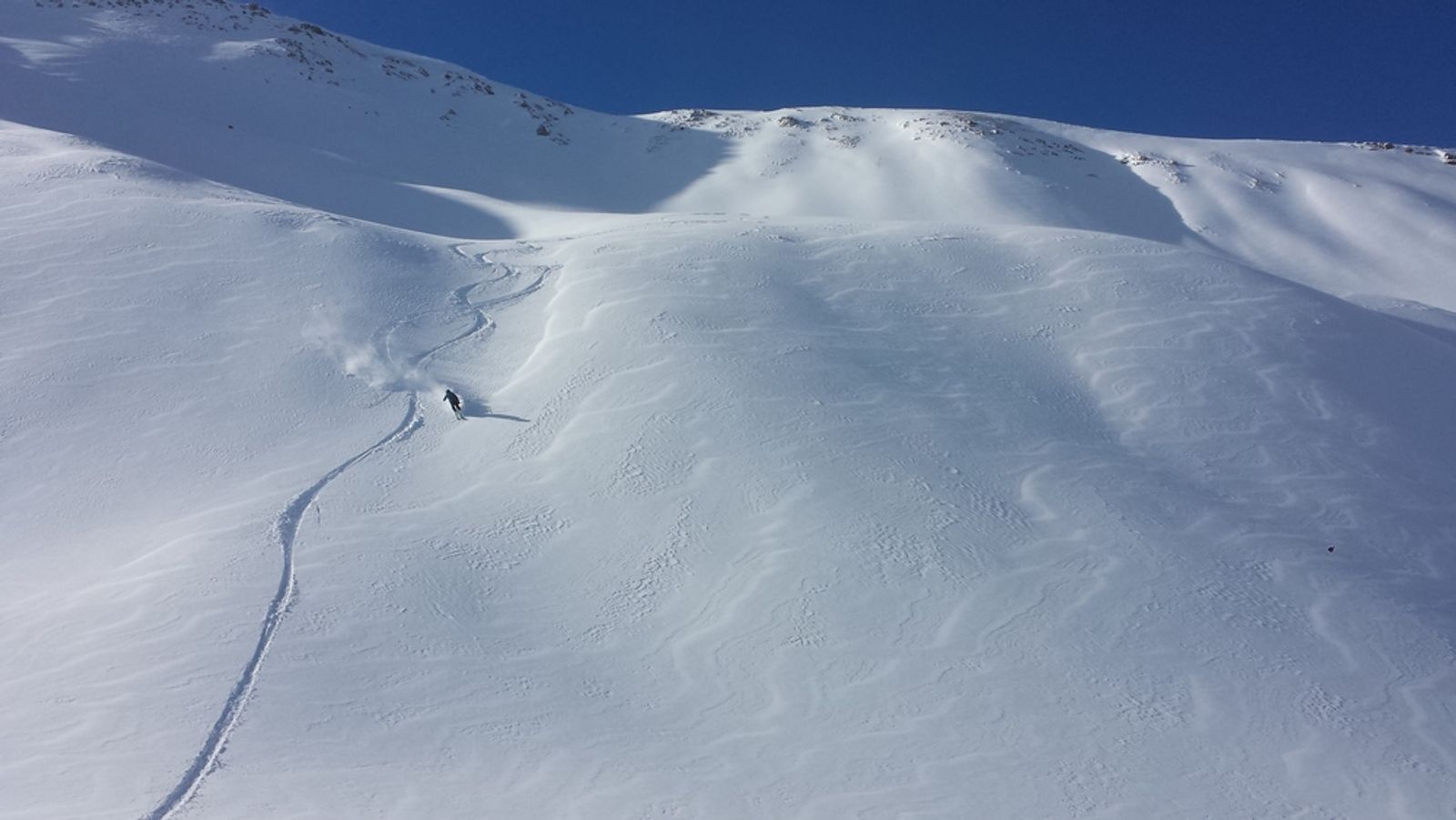 Traces de descente et skieur dans une combe enneigée de la Tête du Crachet.