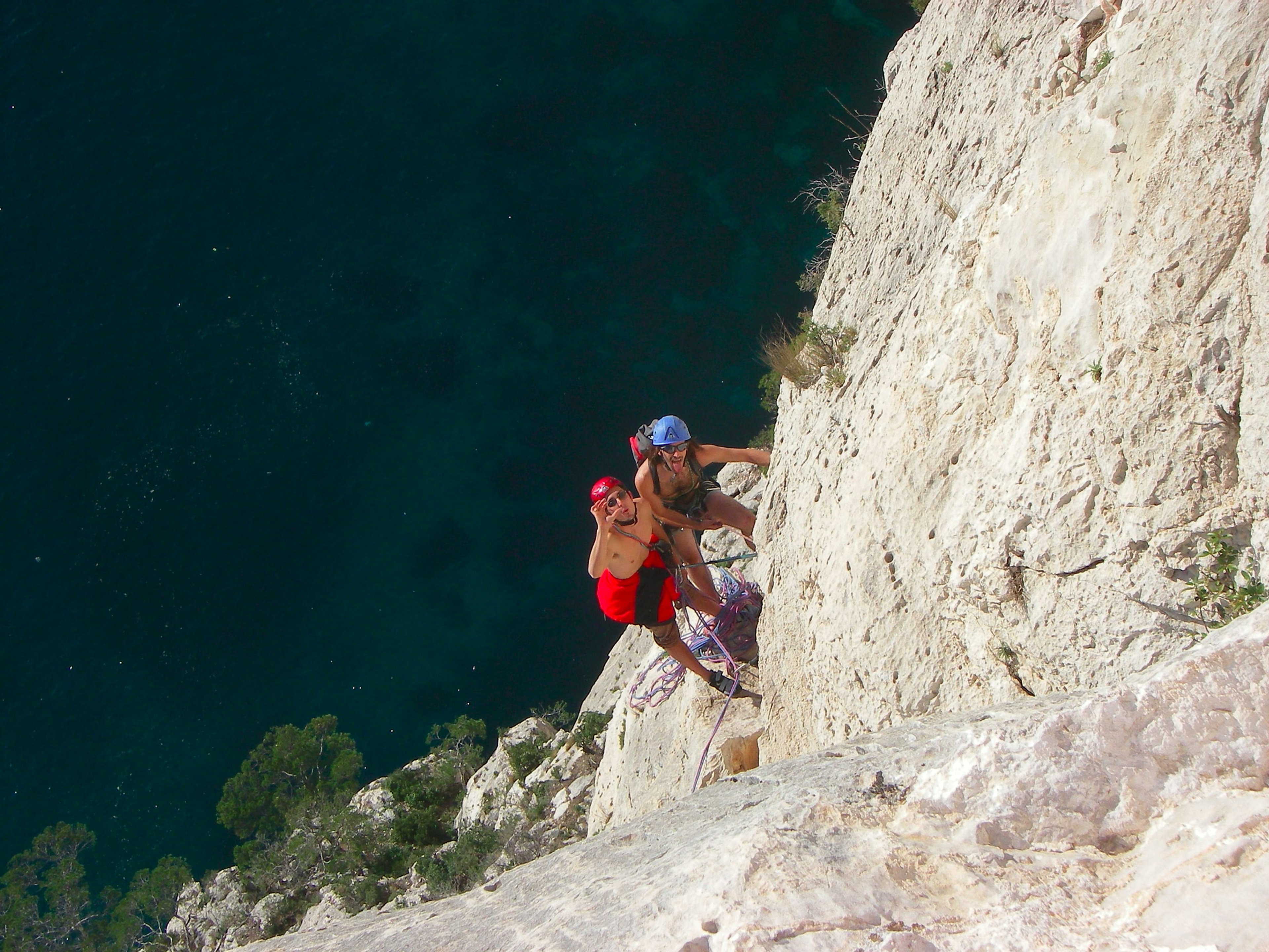 Grimpeur avec un sac à dos dans une grande voie calcaire au-dessus de la mer dans les Calanques.