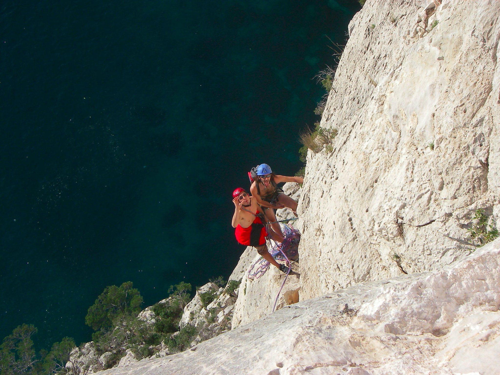 Grimpeur avec un sac à dos dans une grande voie calcaire au-dessus de la mer dans les Calanques.