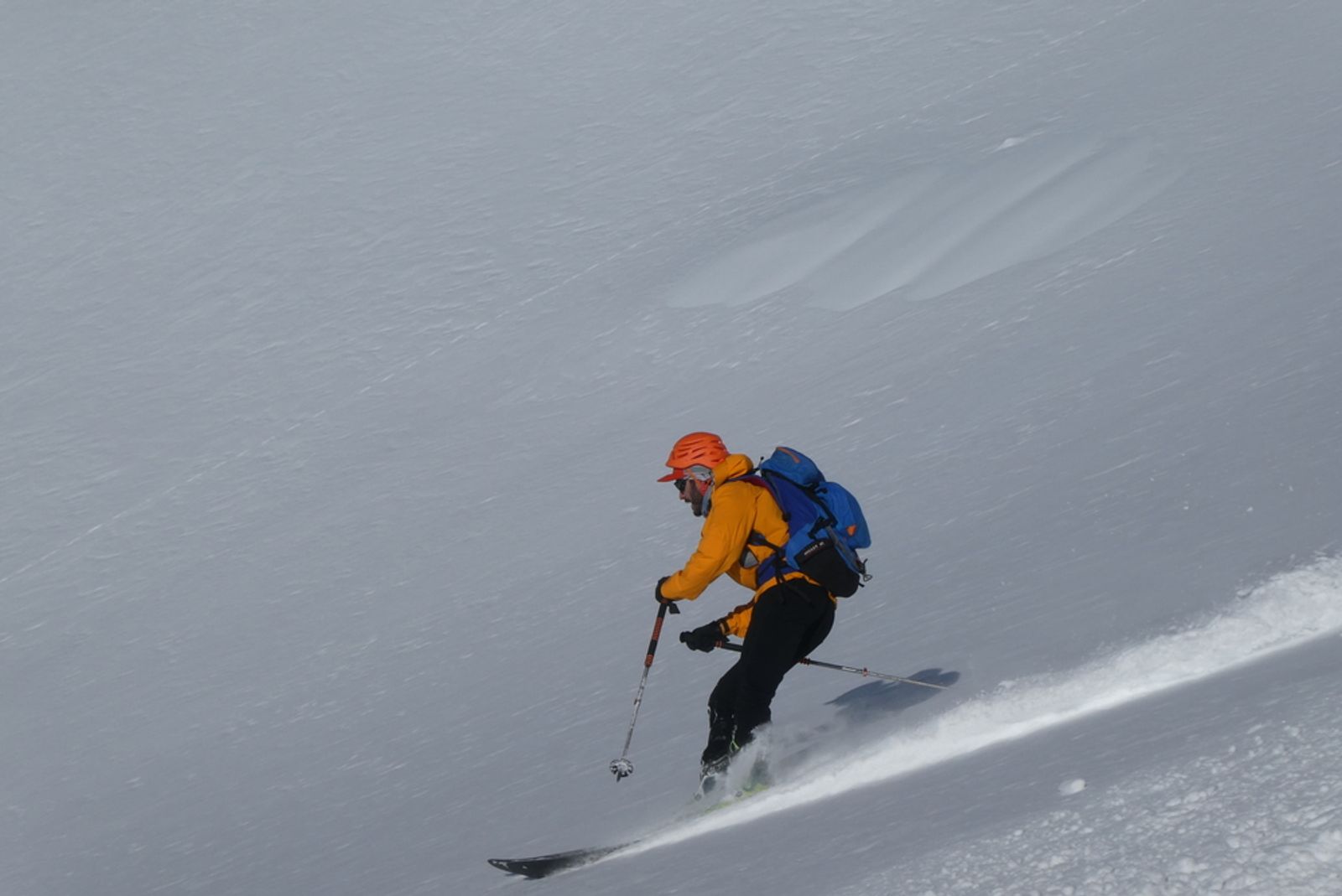 Antoine en veste orange enchaîne un virage dans la poudreuse du Ravin Noir.