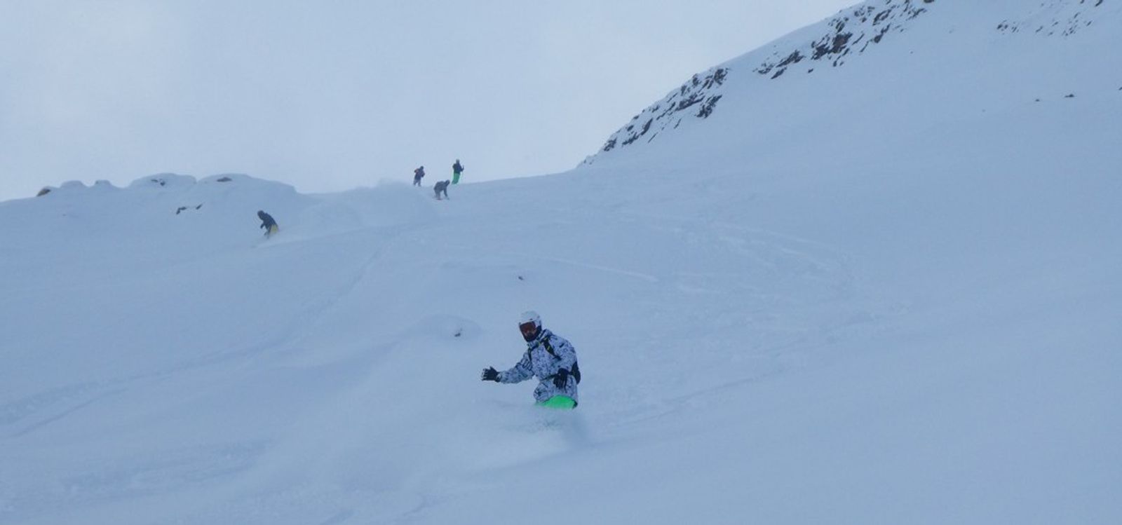 Snowboardeur au premier plan et autres riders sur une pente de neige fraîche à La Grave.