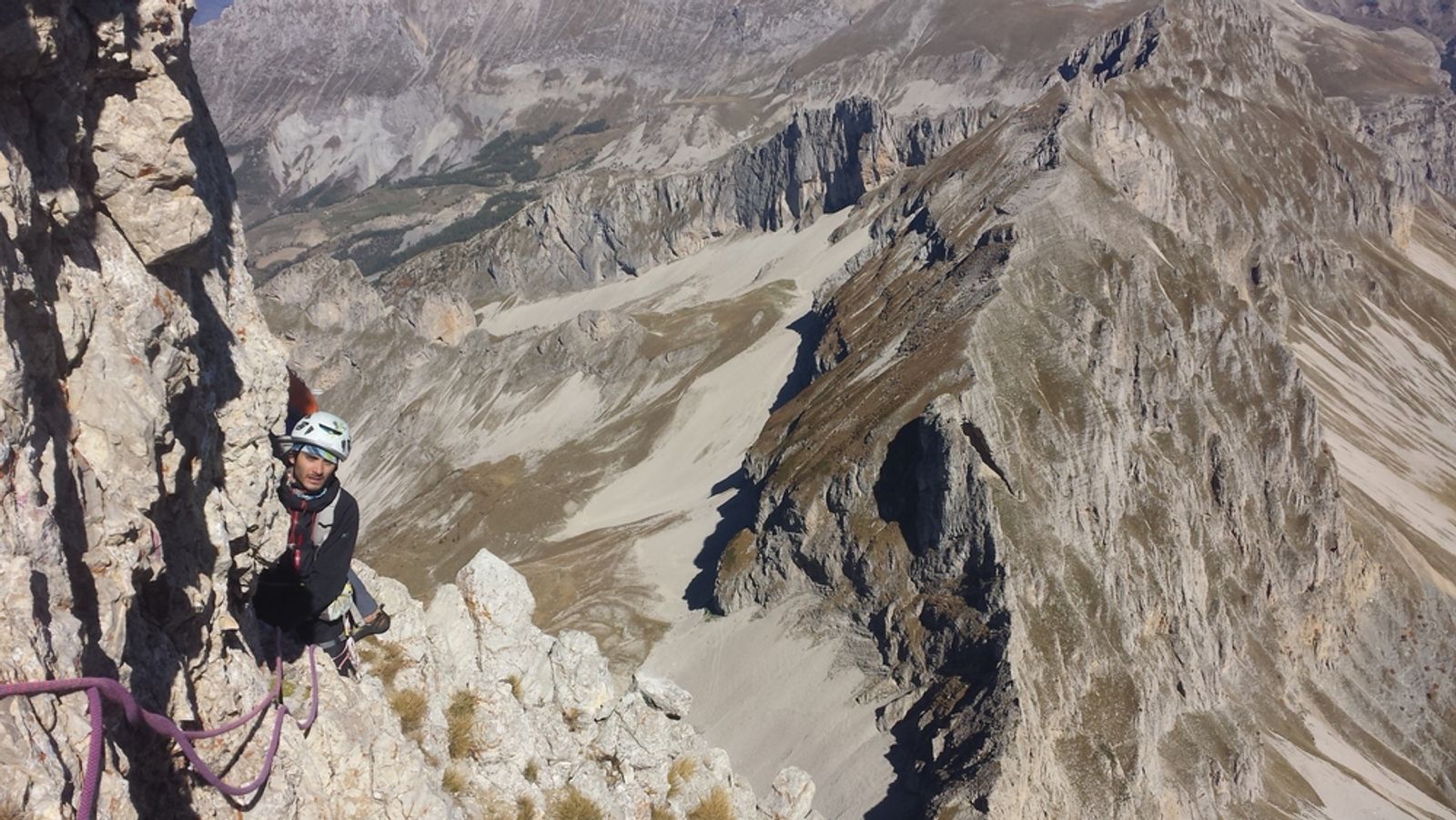 Grimpeur dans le haut de la voie Desmaison, avec les falaises et les pierriers du Dévoluy en arrière-plan