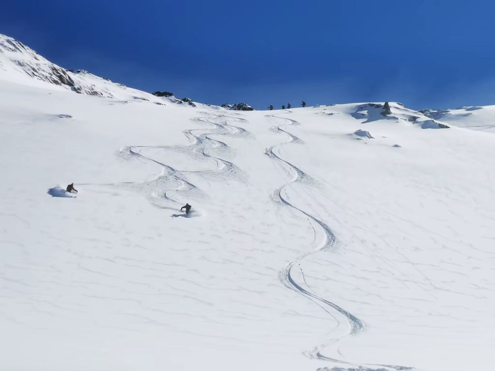 Skieurs descendant une pente de neige fraîche sous le ciel bleu du Groenland