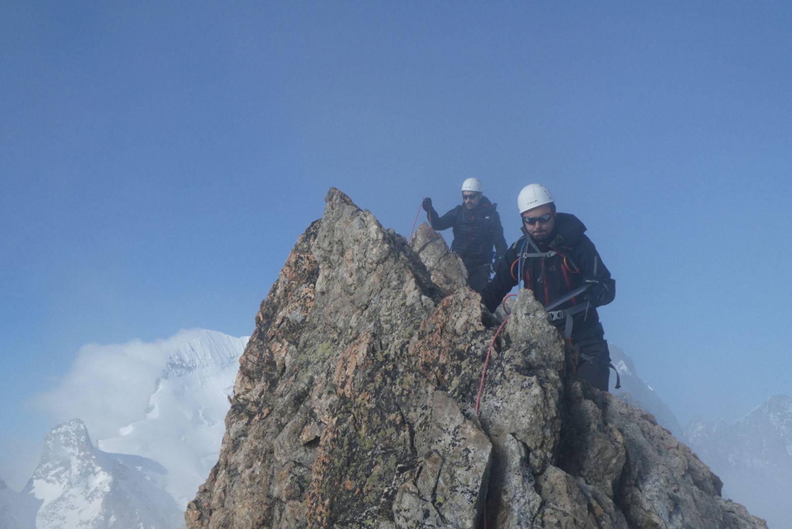Deux alpinistes encordés sur une arête rocheuse, dans une brume légère, vers la fin de la traversée.