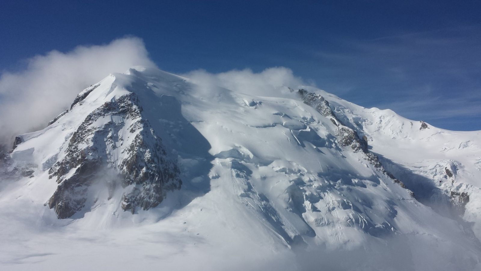 Vue vers le Mont-Blanc depuis l’arête des Cosmiques, avec les faces enneigées et les nuages accrochés aux sommets.