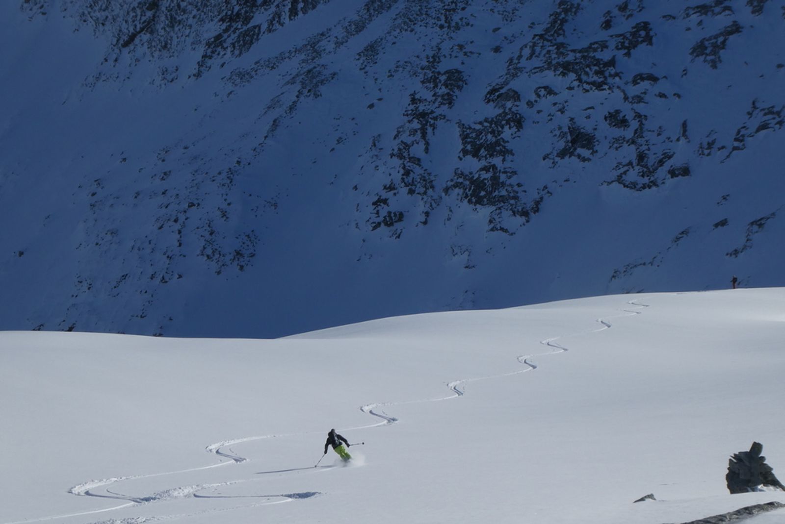 Skieur en pantalon vert traçant dans la poudreuse sous le col d’Aussois.