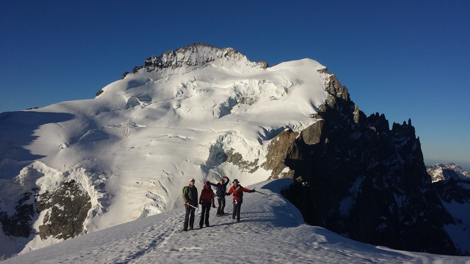 Groupe d’alpinistes sur une crête enneigée de Roche Faurio, face au Dôme des Écrins.