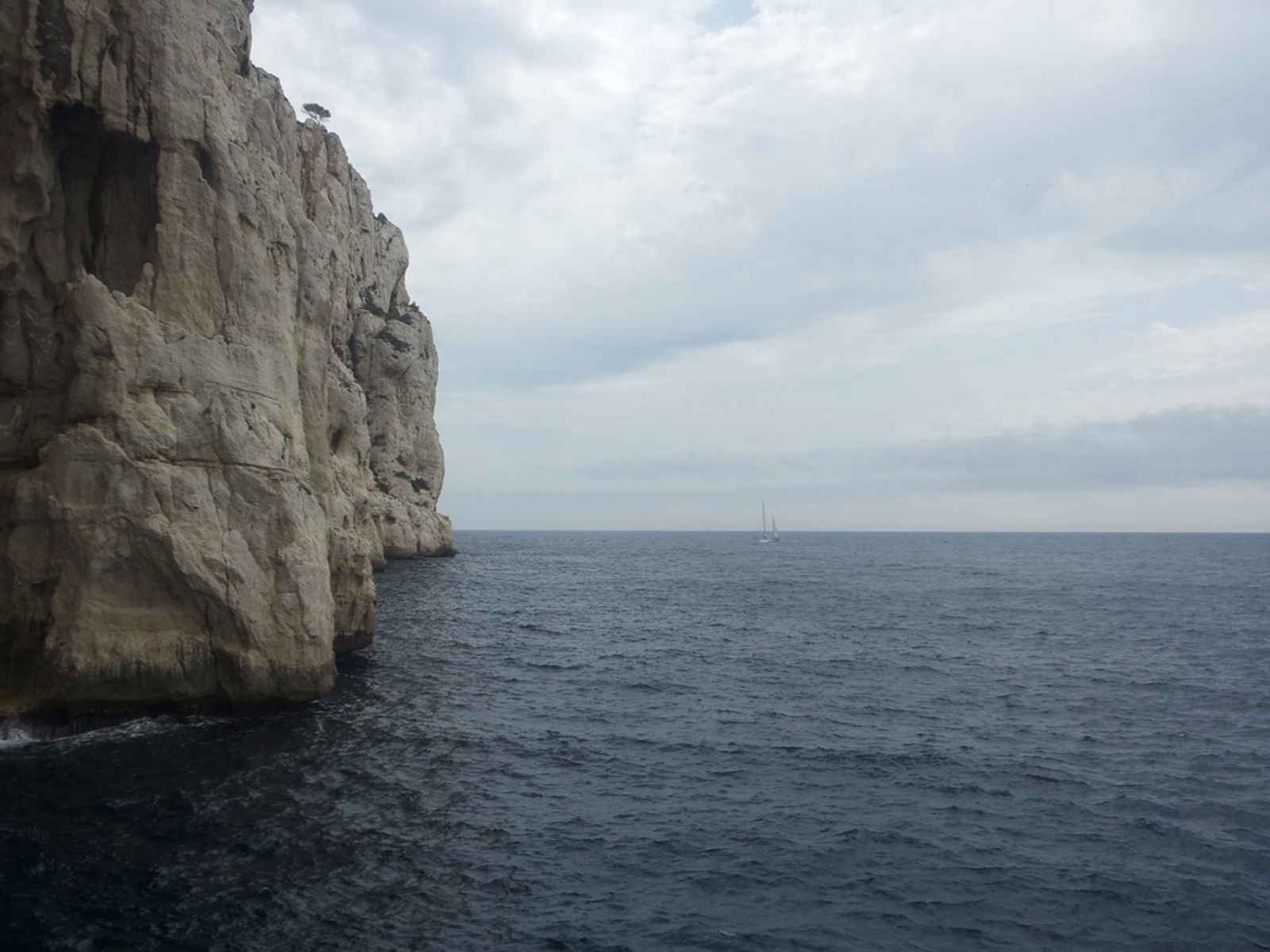 Falaise calcaire de Castelvieil tombant dans la mer sous un ciel nuageux