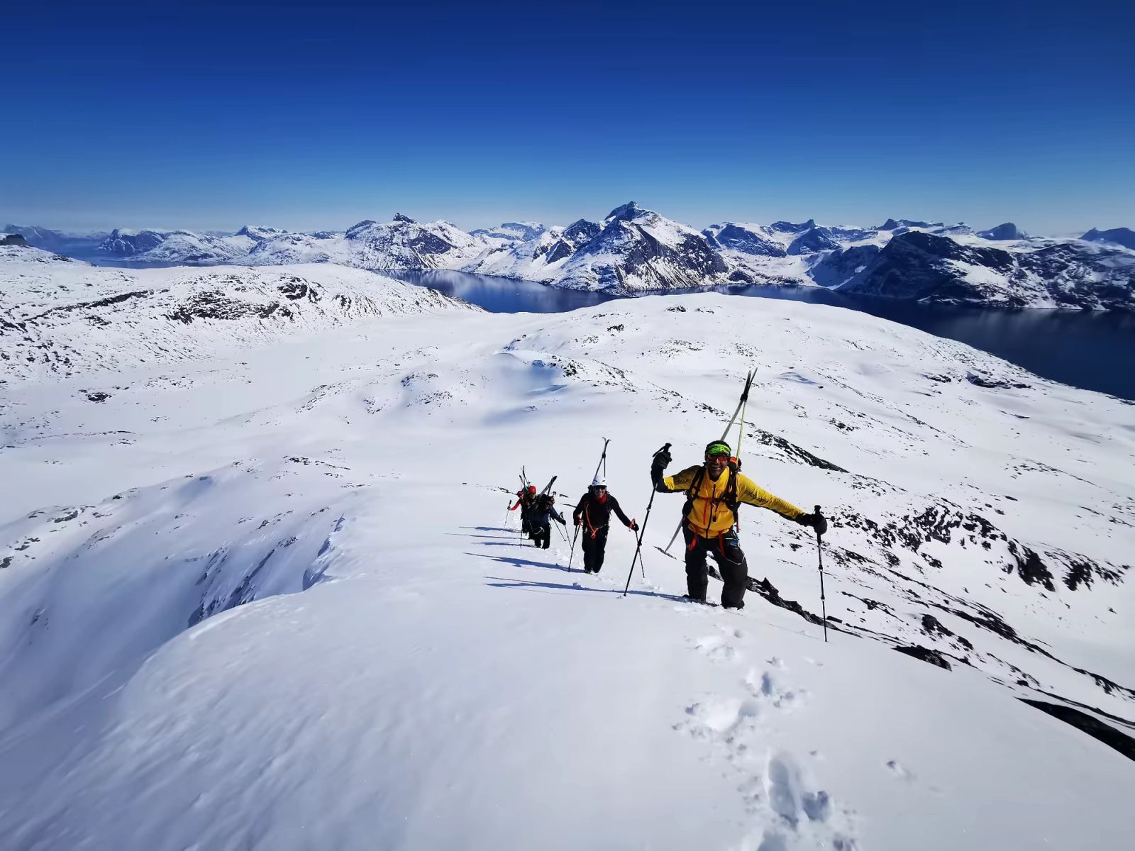 Randonneurs skis sur le sac sur une crête avec un panorama de montagnes enneigées au Groenland