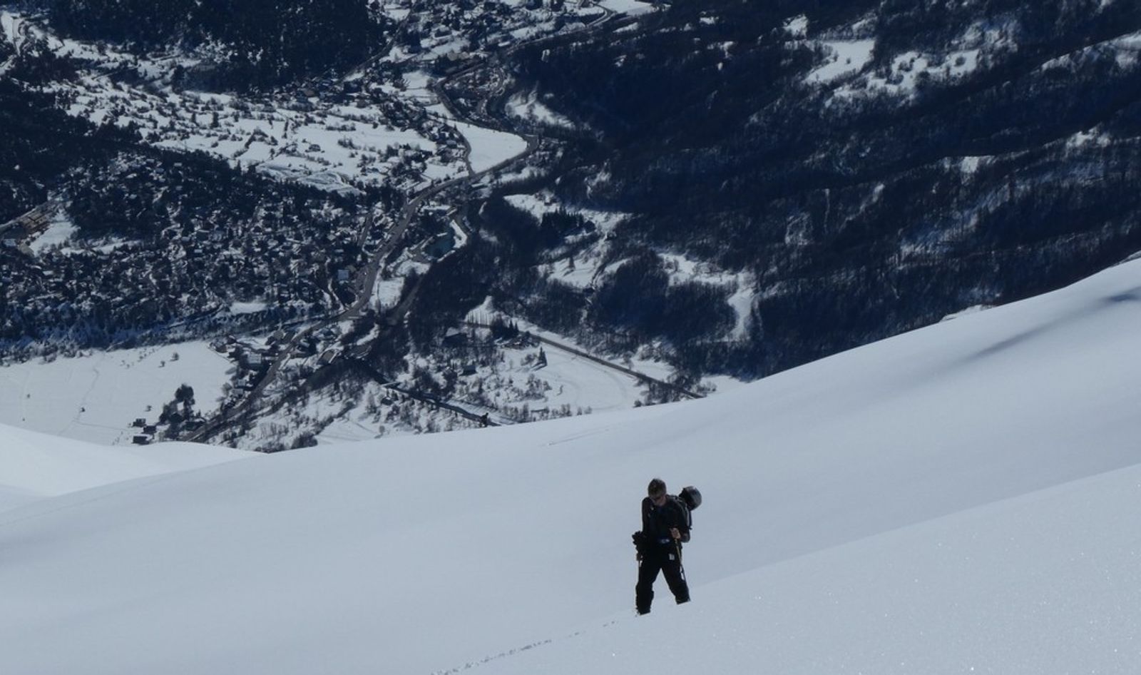 A skier walking through the snow, with the village of Vallouise in the background