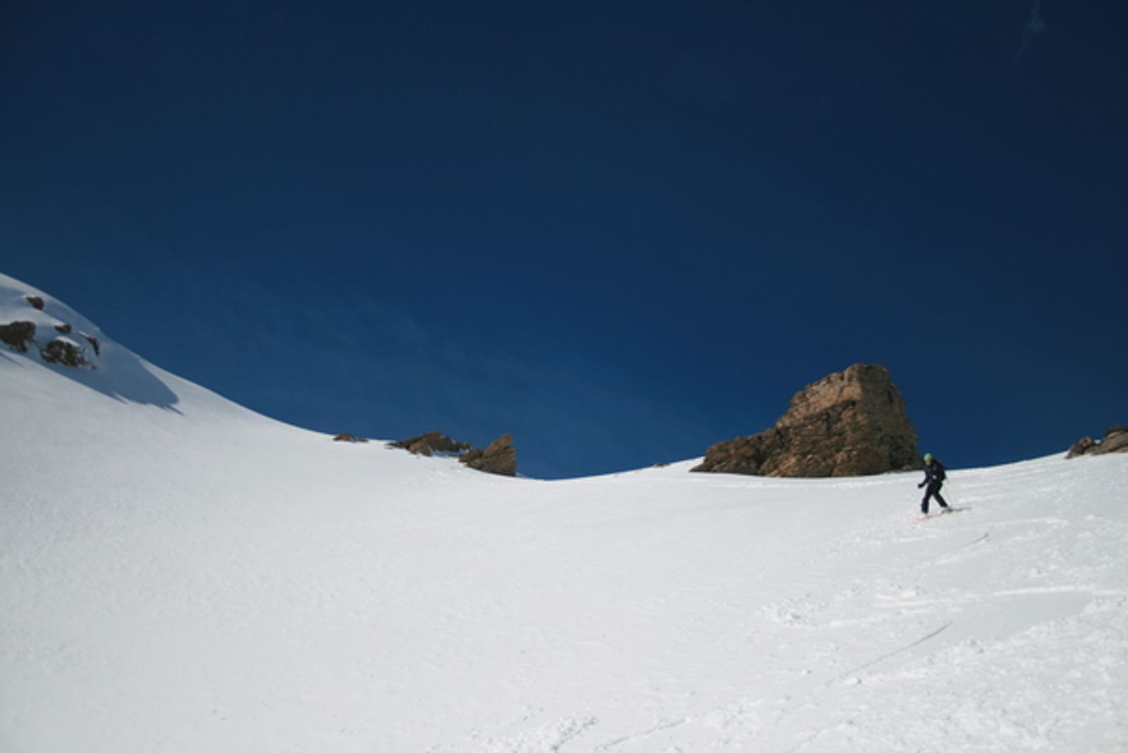 Skieur descendant une pente enneigée bordée de rochers sur le versant sud-est du Girardin.