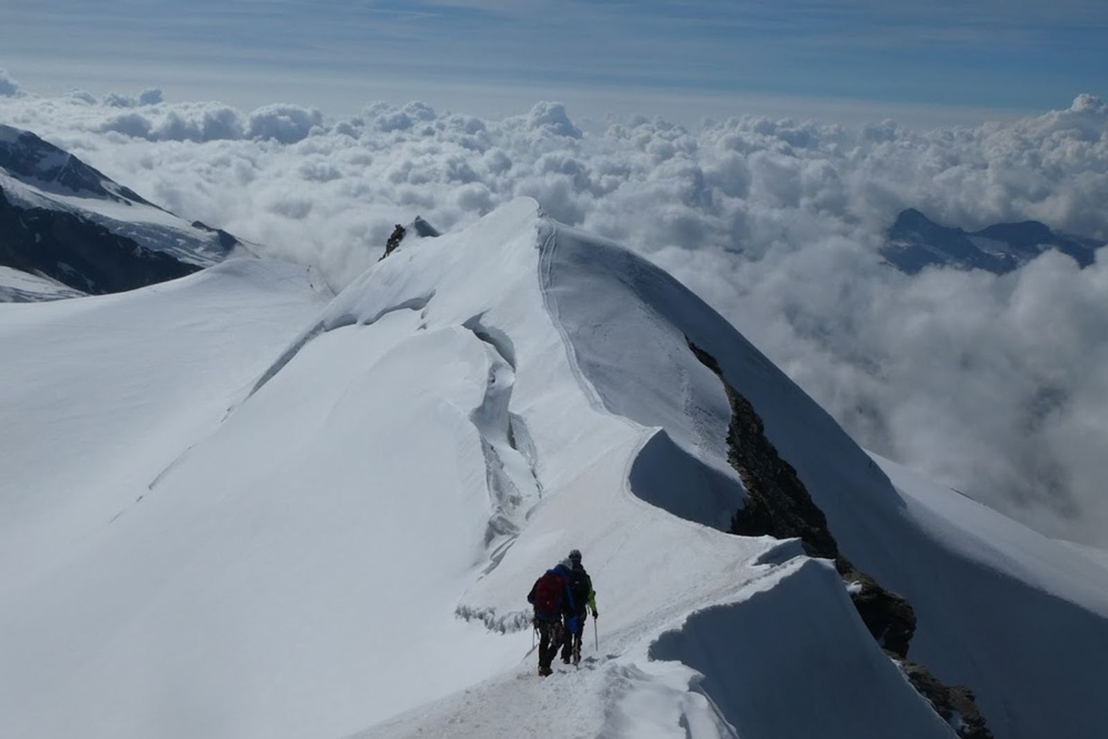 Alpiniste progressant sur l’arête effilée de Castor, entre neige et nuages.