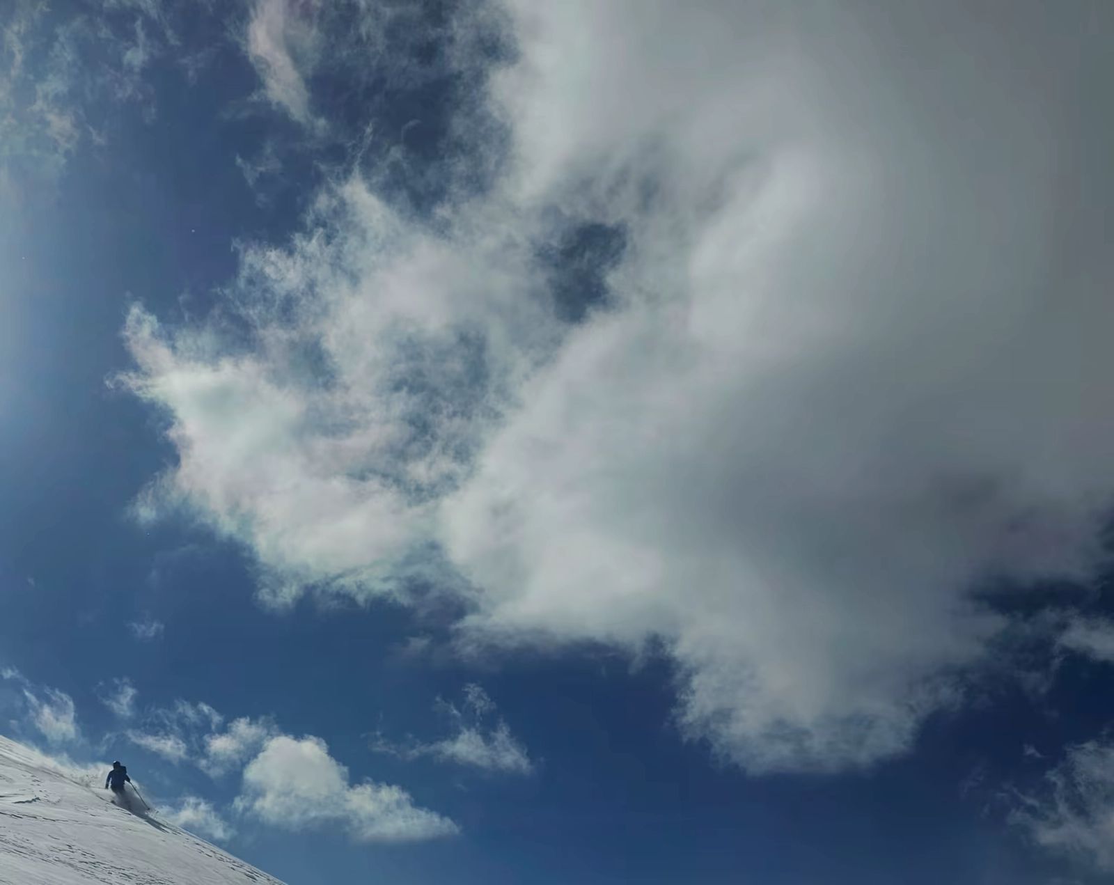 Petit skieur dans un coin de la photo avec un beau nuage et du ciel bleu