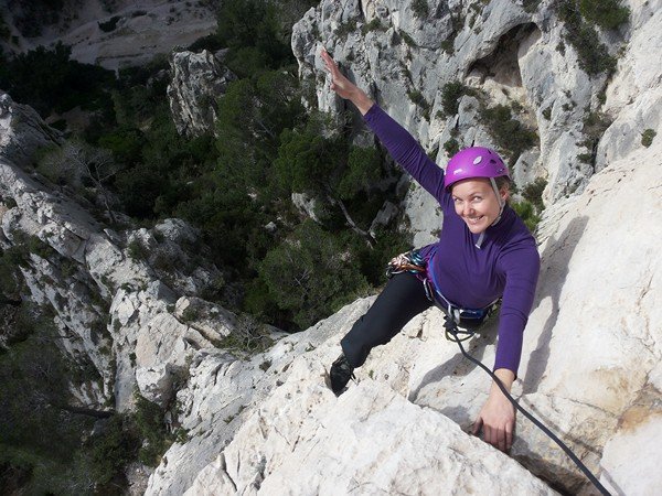 Grimpeuse souriante en haut violet levant un bras sur la paroi de la Saphir
