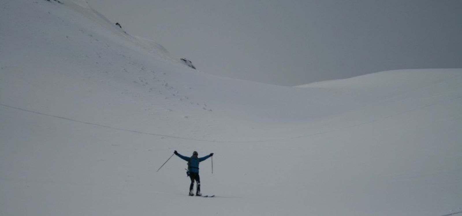 A skier standing still, arms raised, in a snow-covered valley at the Cime du Grand Vallon.
