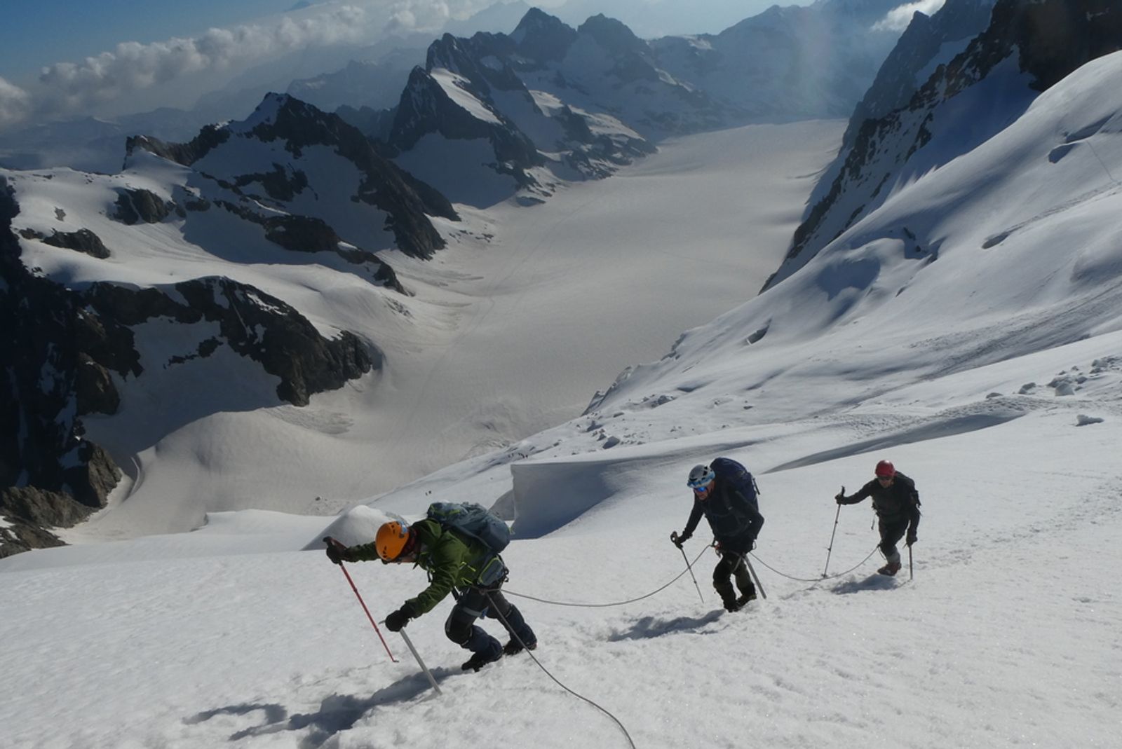Trois alpinistes encordés remontent une pente de neige sur le Dôme des Écrins.