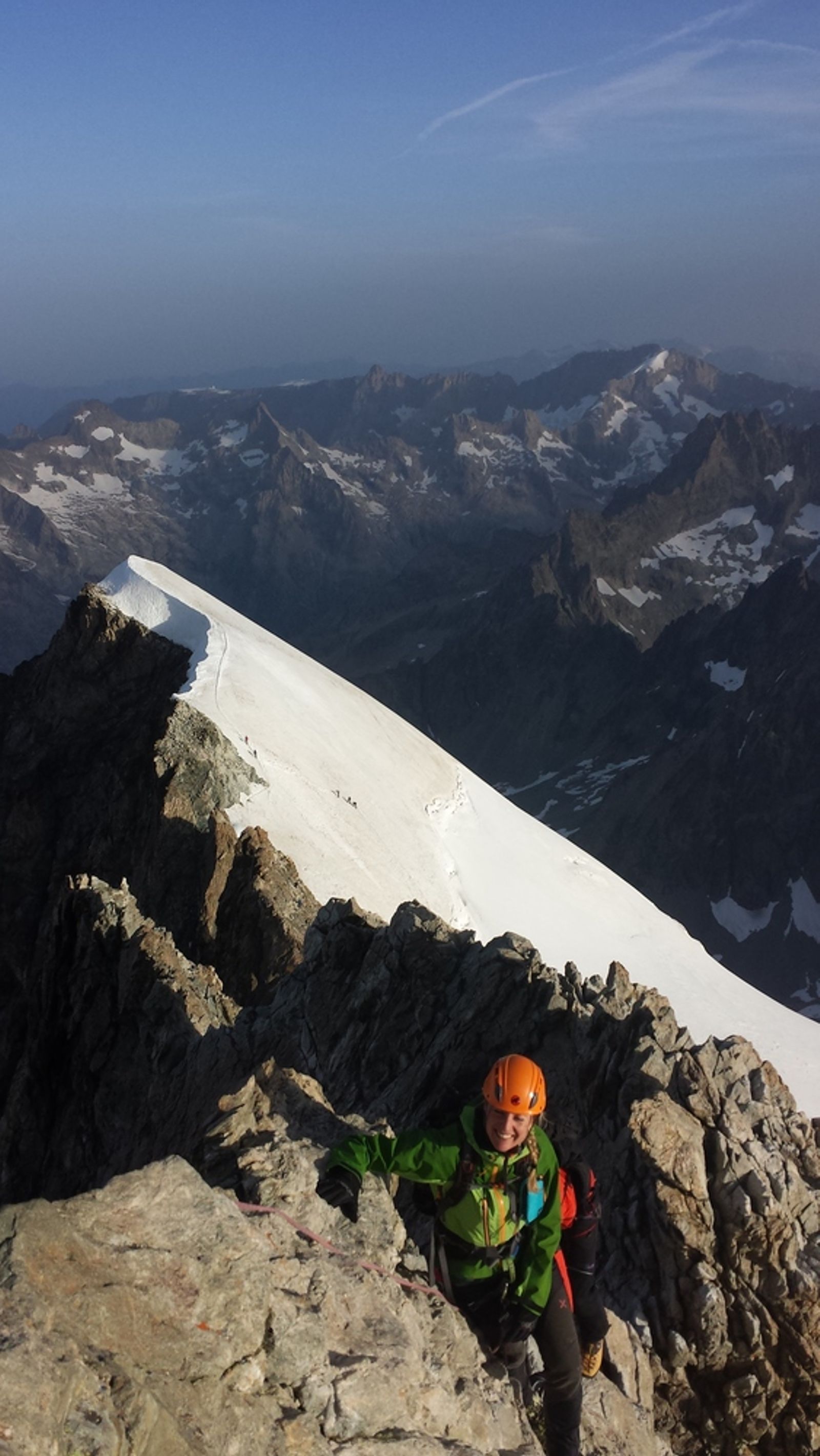 Une participante gravit les rochers de la Barre des Écrins, à côté de l’arête enneigée.