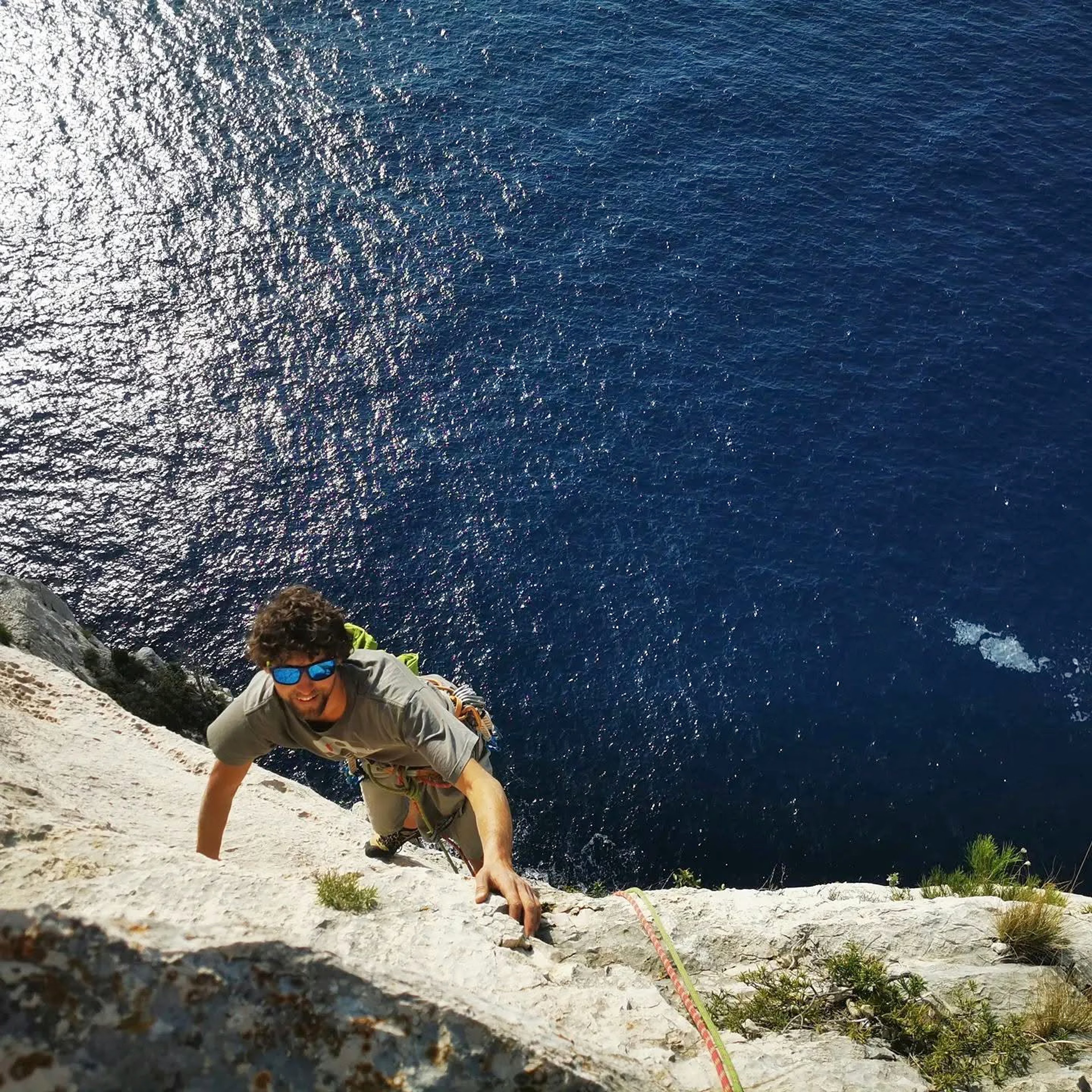 Grimpeur encordé sur une paroi calcaire au-dessus de la Méditerranée dans les Calanques.