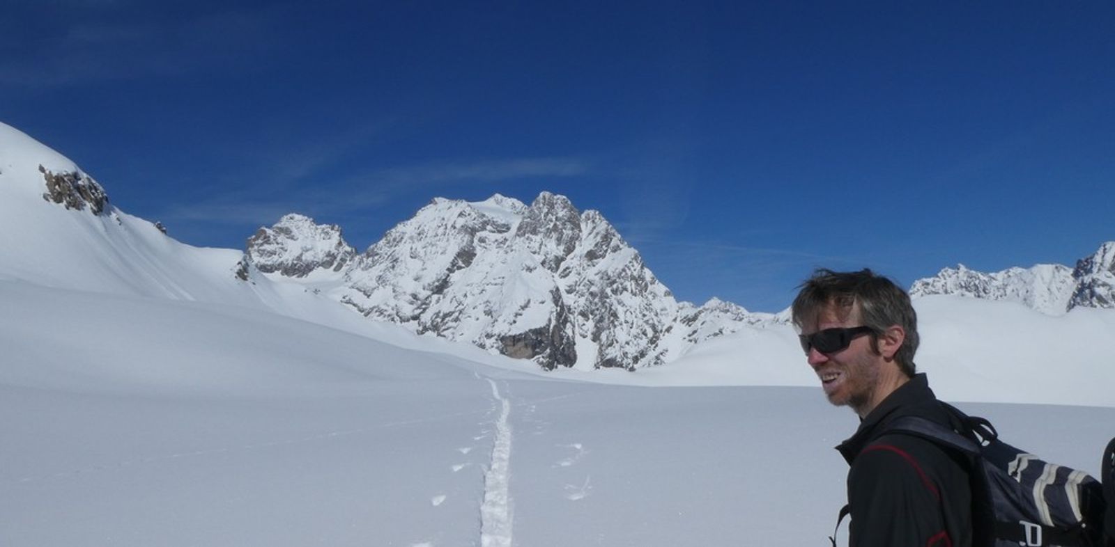 Close-up of a skier with the Pelvoux and the Unnamed Peak, blanketed in snow, in the background