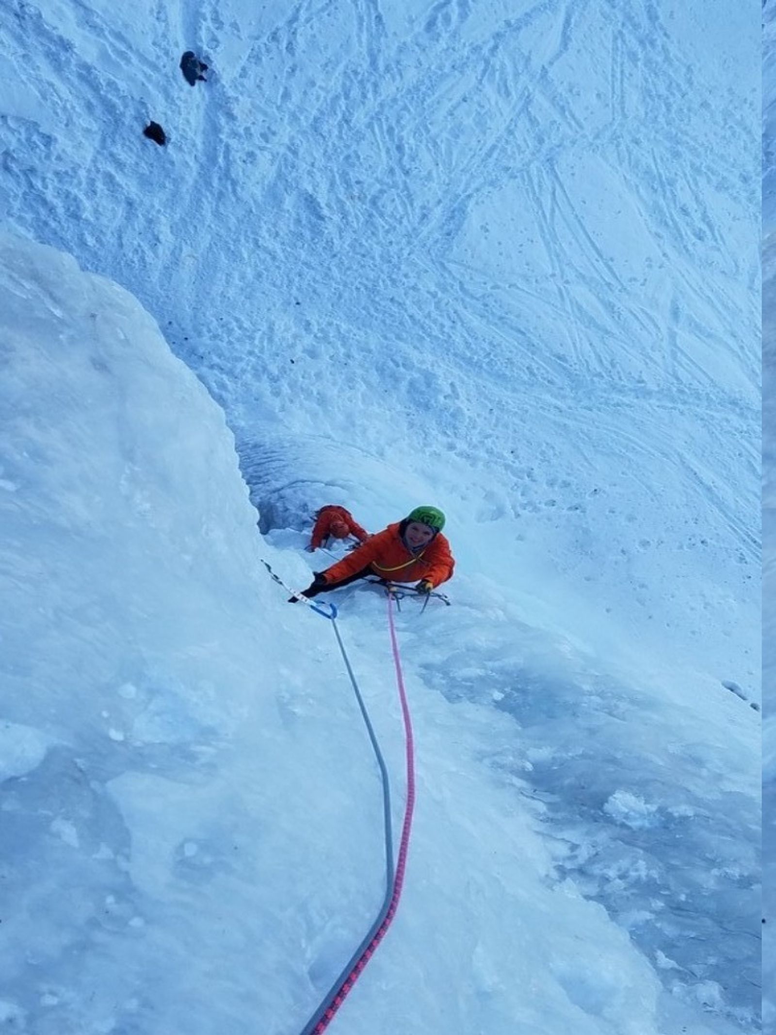 Grimpeur en haut d’une cascade de glace encaissée entre les rochers du Val Argentera.