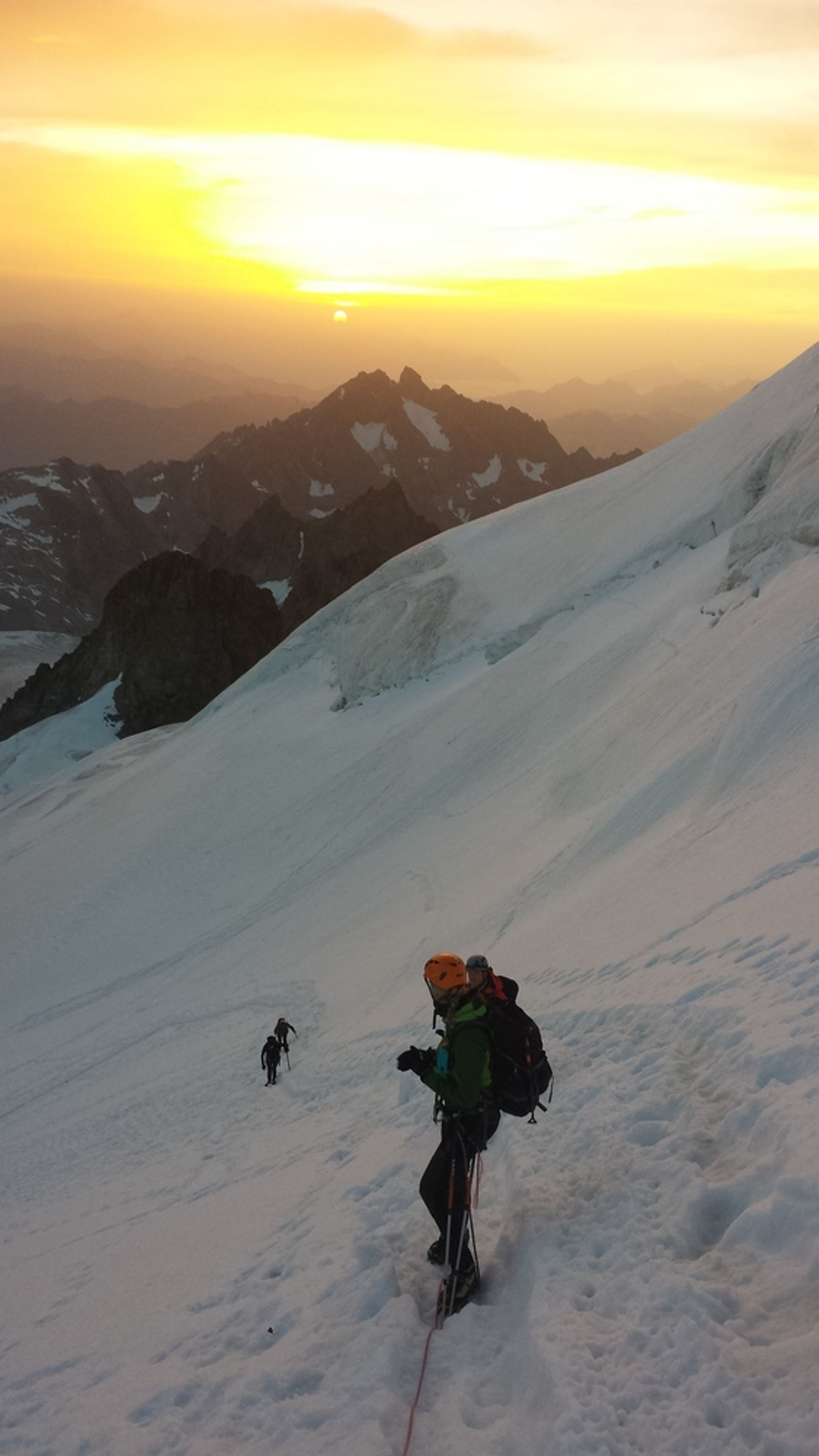 La cordée remonte une pente enneigée vers la Barre des Écrins dans la lumière du lever du soleil.