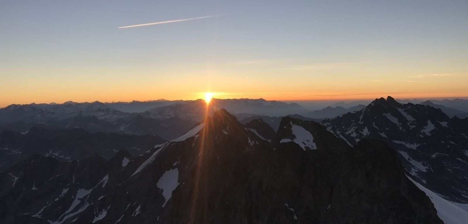 Le soleil apparaît à l’horizon au-dessus des montagnes, vu depuis le sommet de Roche Faurio.
