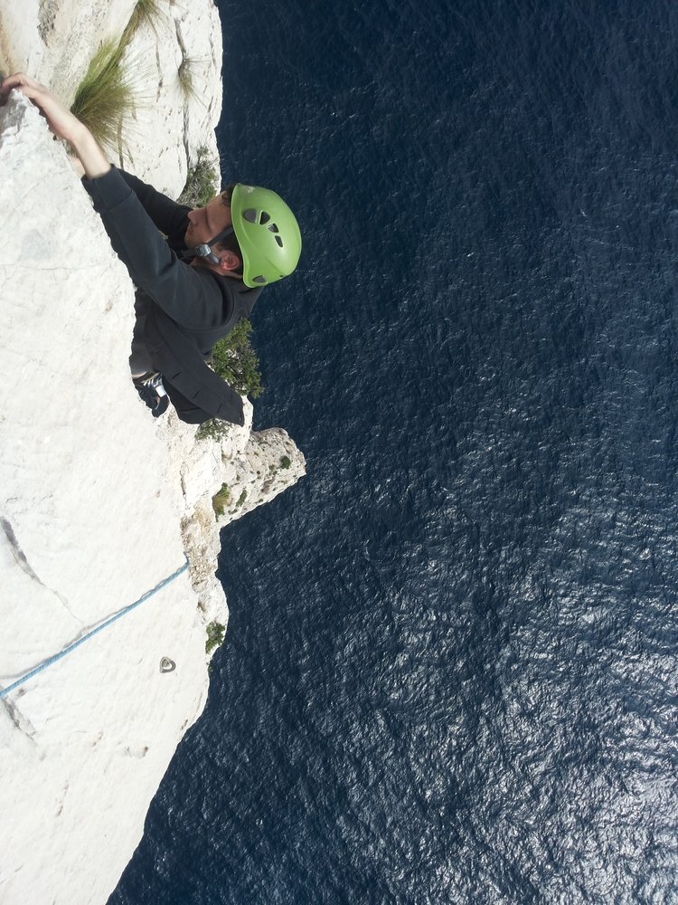 Grimpeur au casque vert sur une paroi blanche dominant directement la mer