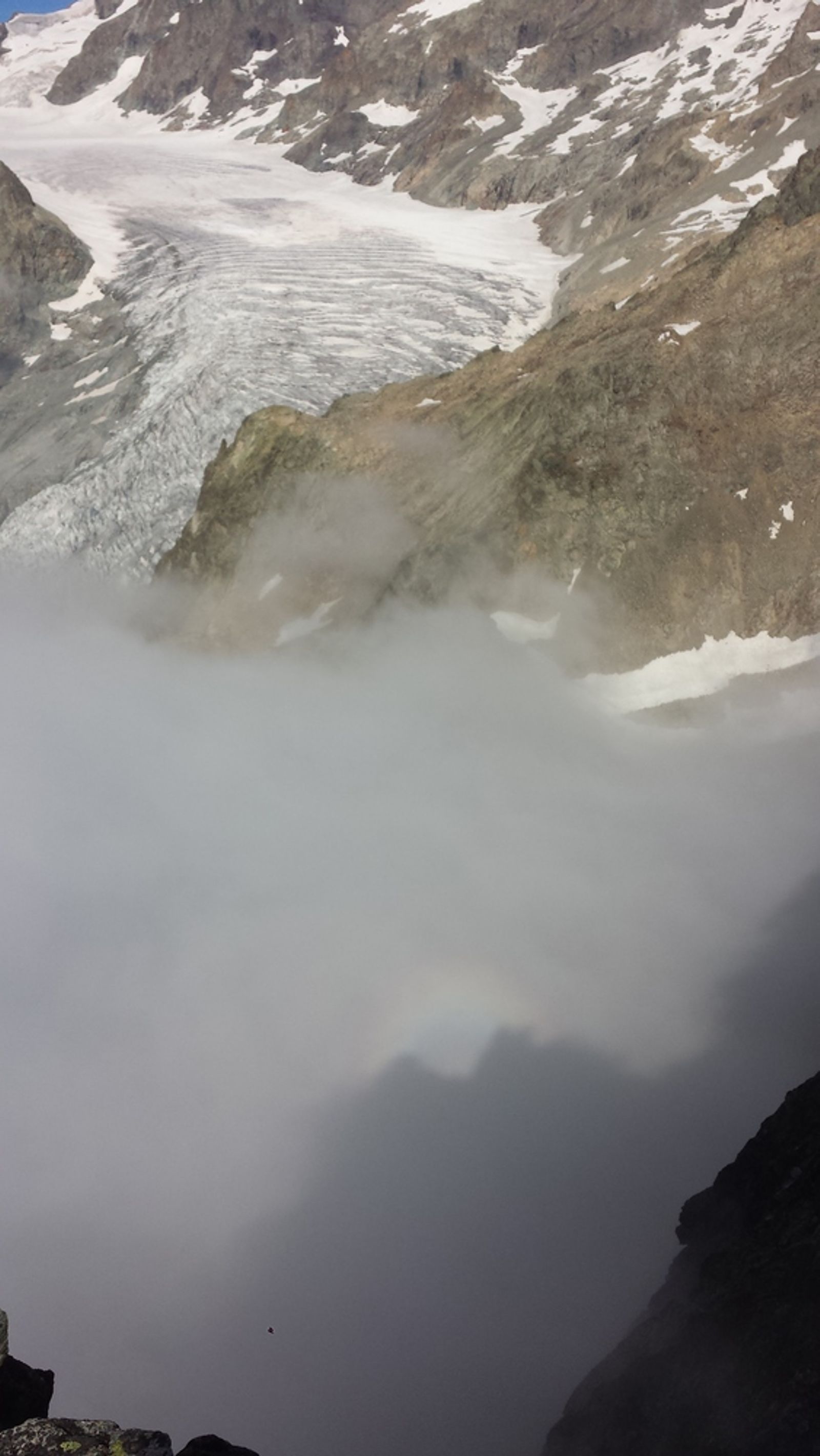 Une ombre se dessine dans les nuages sous les rochers de l’arête des Cinéastes.