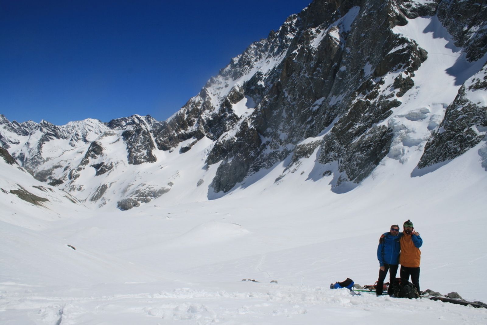 Two skiers at a standstill on the Glacier Noir, facing the Écrins cliffs.