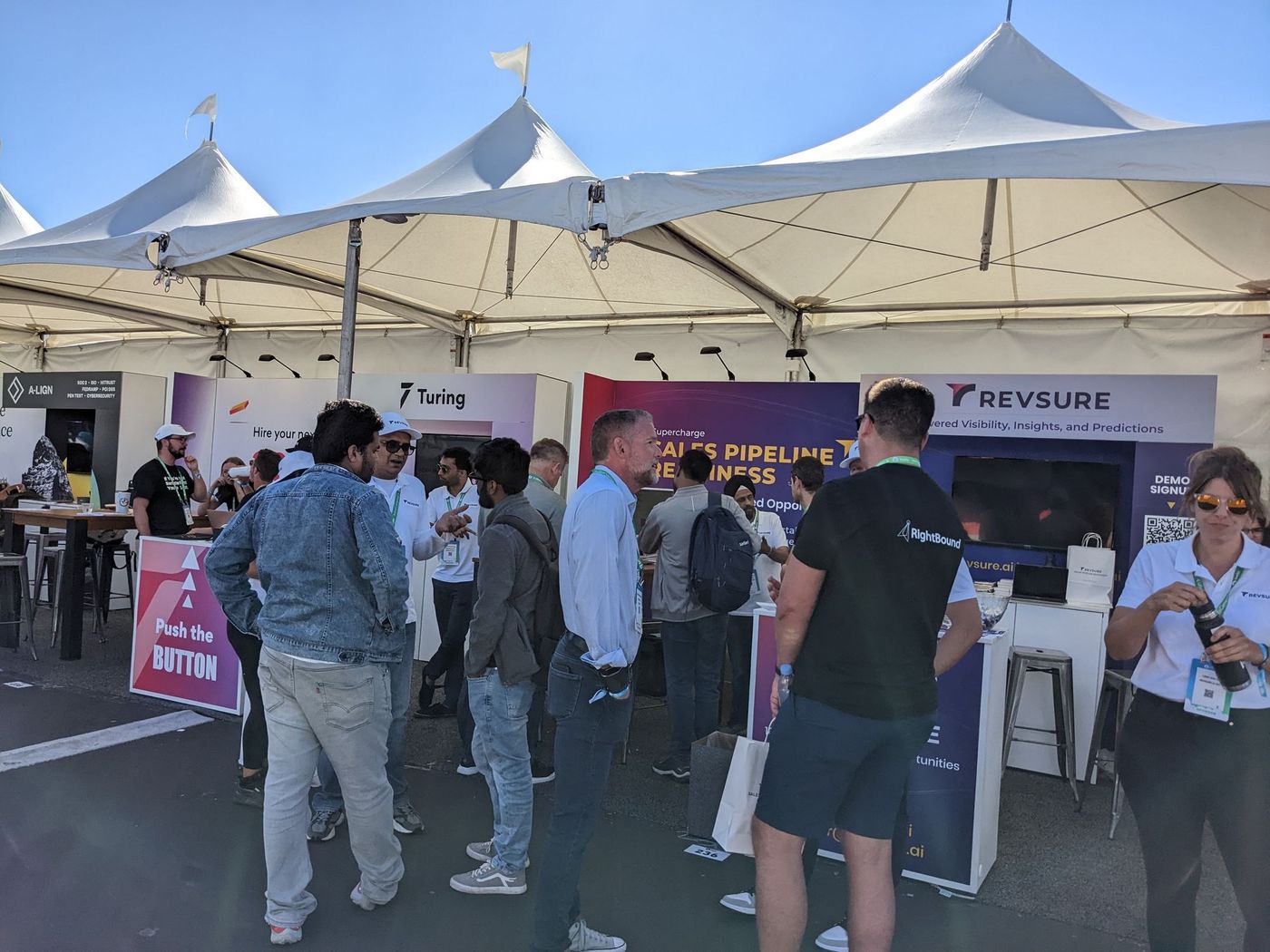 People gathered at an outdoor event under a tent with a Revsure booth.