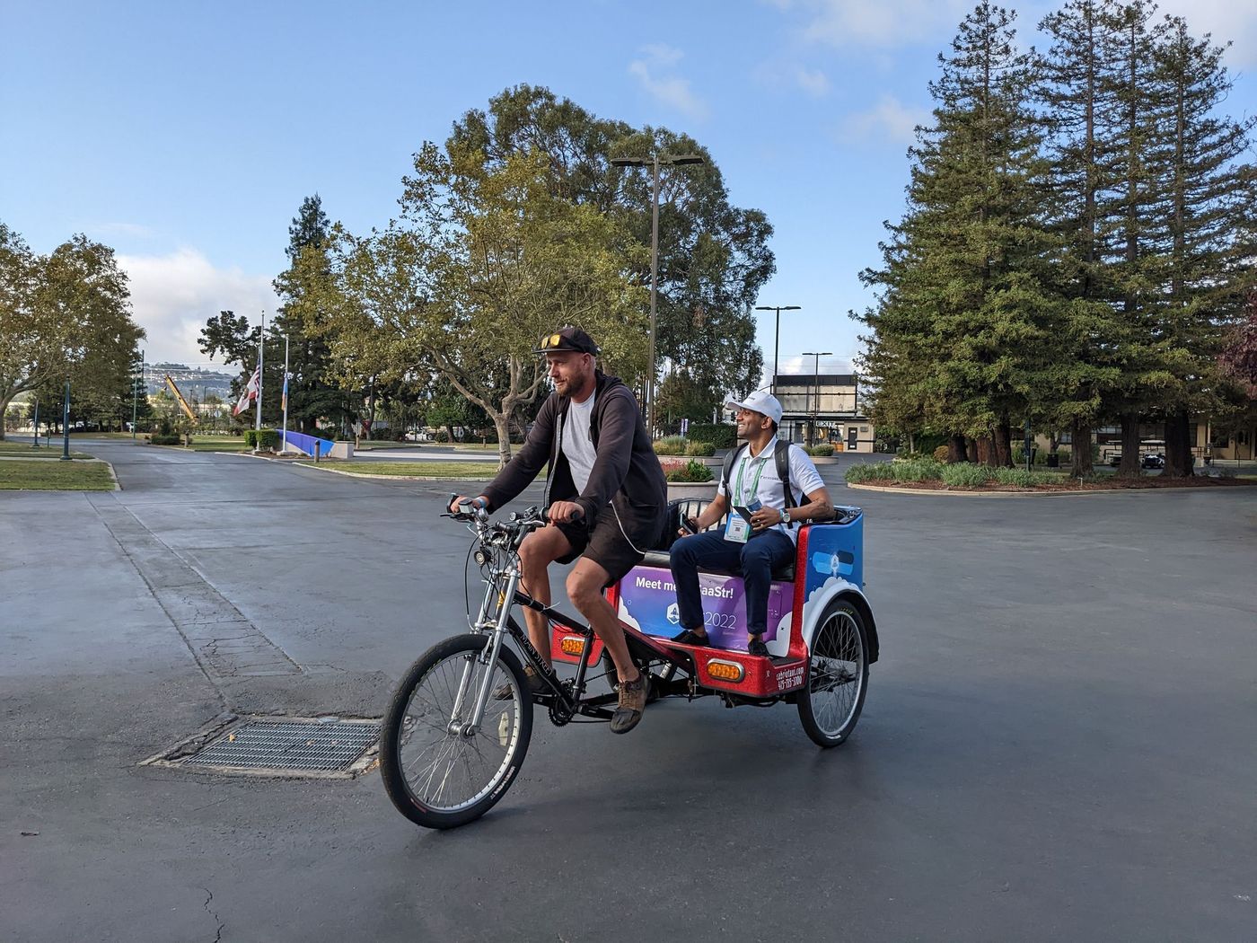 Two men riding a red tricycle with advertisements on the side.