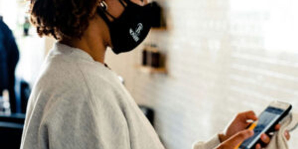 A lady in a facemask making a payment on her mobile phone