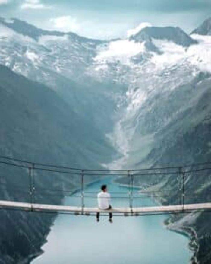 Person sitting on a bridge overlooking the Austrian alps