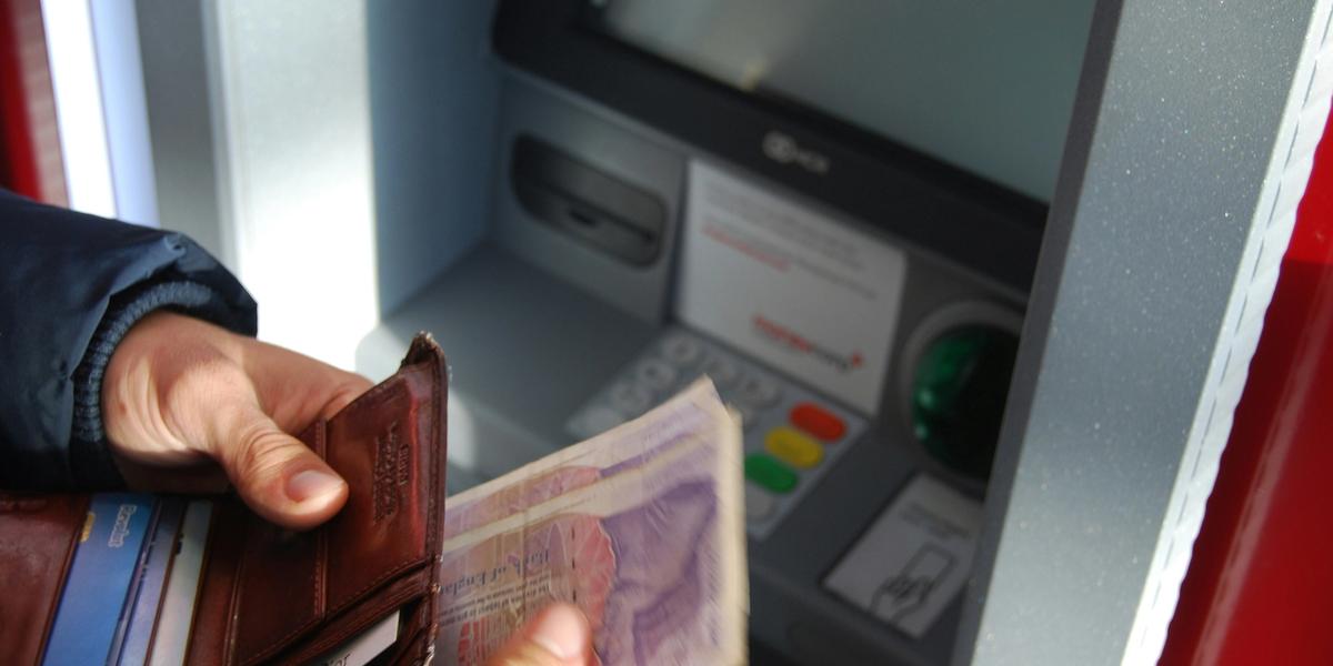 person holding brown leather wallet and banknotes in front of an ATM