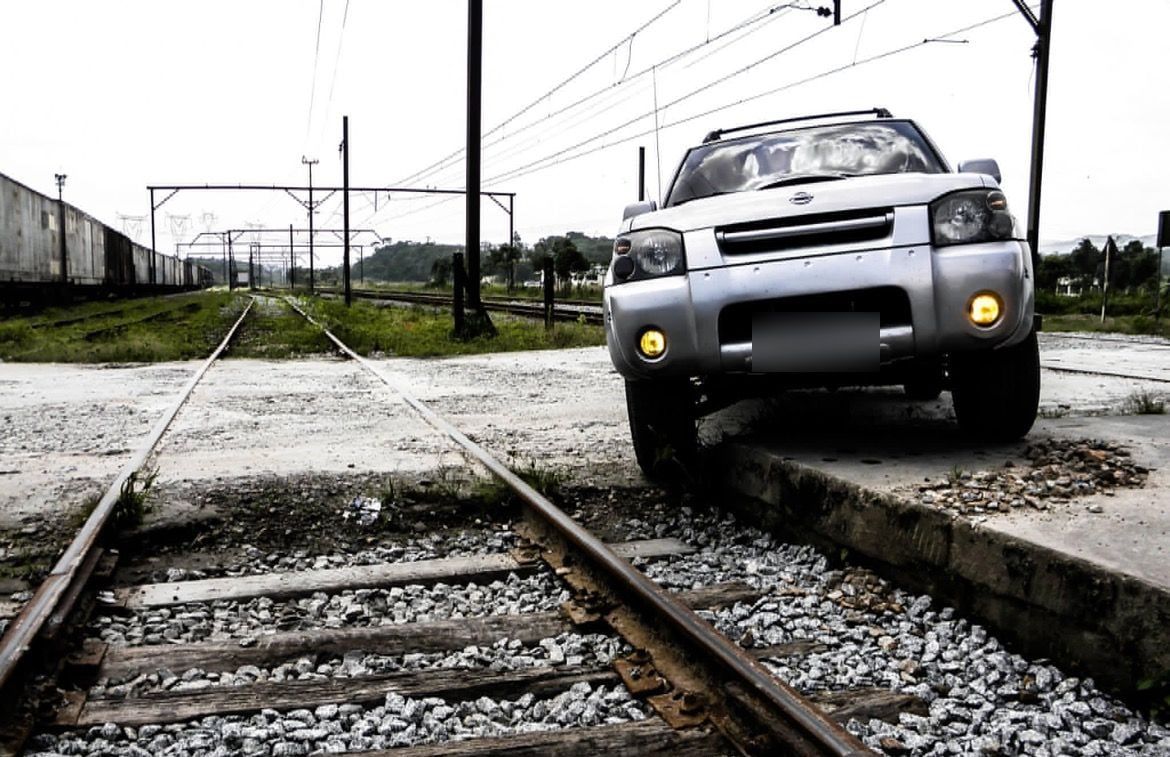 Picape Nissan Frontier prata com faróis de milha amarelos acesos, parada sobre trilhos de trem