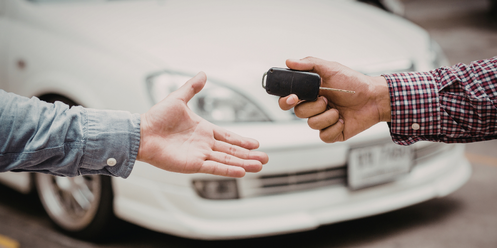 Pessoa entregando chave de carro para outra em frente a veículo, representando finalização da compra de carro usado com segurança e verificação dos dados