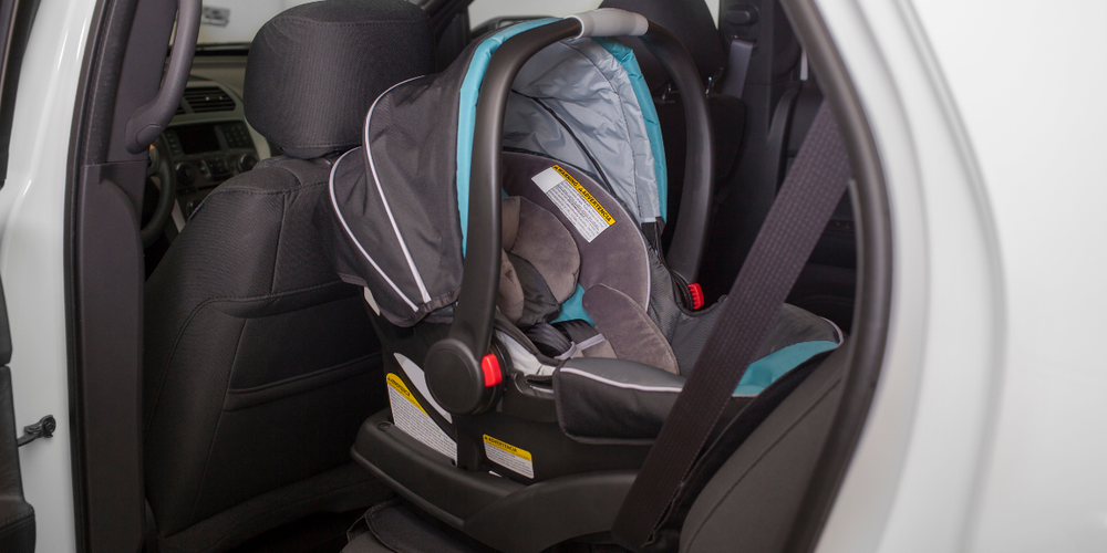 Bebê conforto instalado corretamente no banco traseiro do carro com cinto de segurança, seguindo normas de transporte infantil