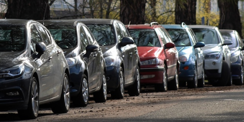 Carros estacionados em fila ao longo de rua arborizada, representando variedade de veículos, mobilidade urbana e opções no mercado automotivo