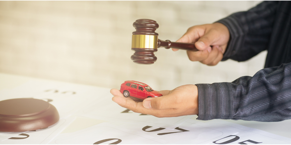 Martelo de juiz sobre miniatura de carro nas mãos, representando leilão de veículos, aspectos legais e compra de carro usado com segurança jurídica