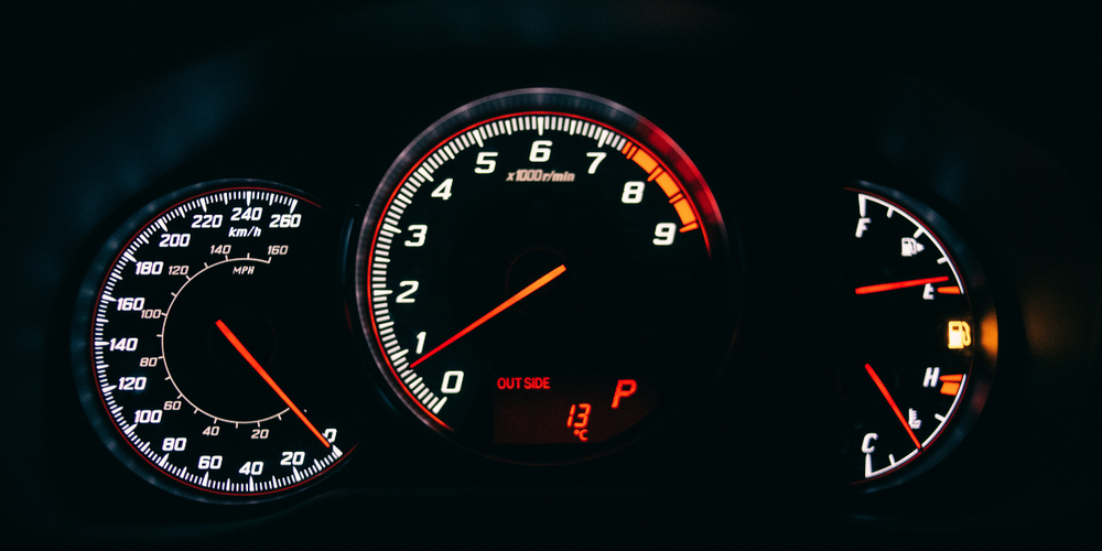 Painel de carro com velocímetro e conta-giros iluminados indicando velocidade e rotação do motor durante condução de veículo