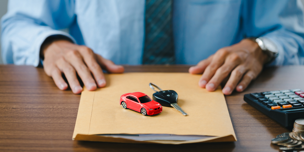 Pessoa analisando documentos de veículo com chave e miniatura de carro sobre a mesa, representando compra, venda e financiamento automotivo